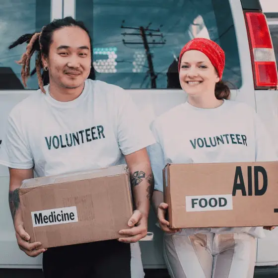 2 volunteers holding medical and food boxes behind a van